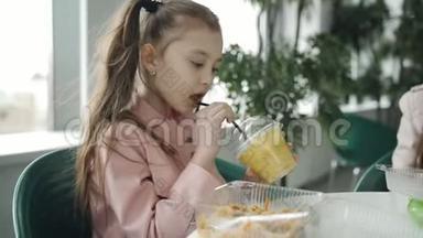 小女孩在咖啡馆里吃面条，<strong>喝</strong>稻草上的胡萝卜汁。 女孩在一个塑料杯里<strong>喝果汁</strong>